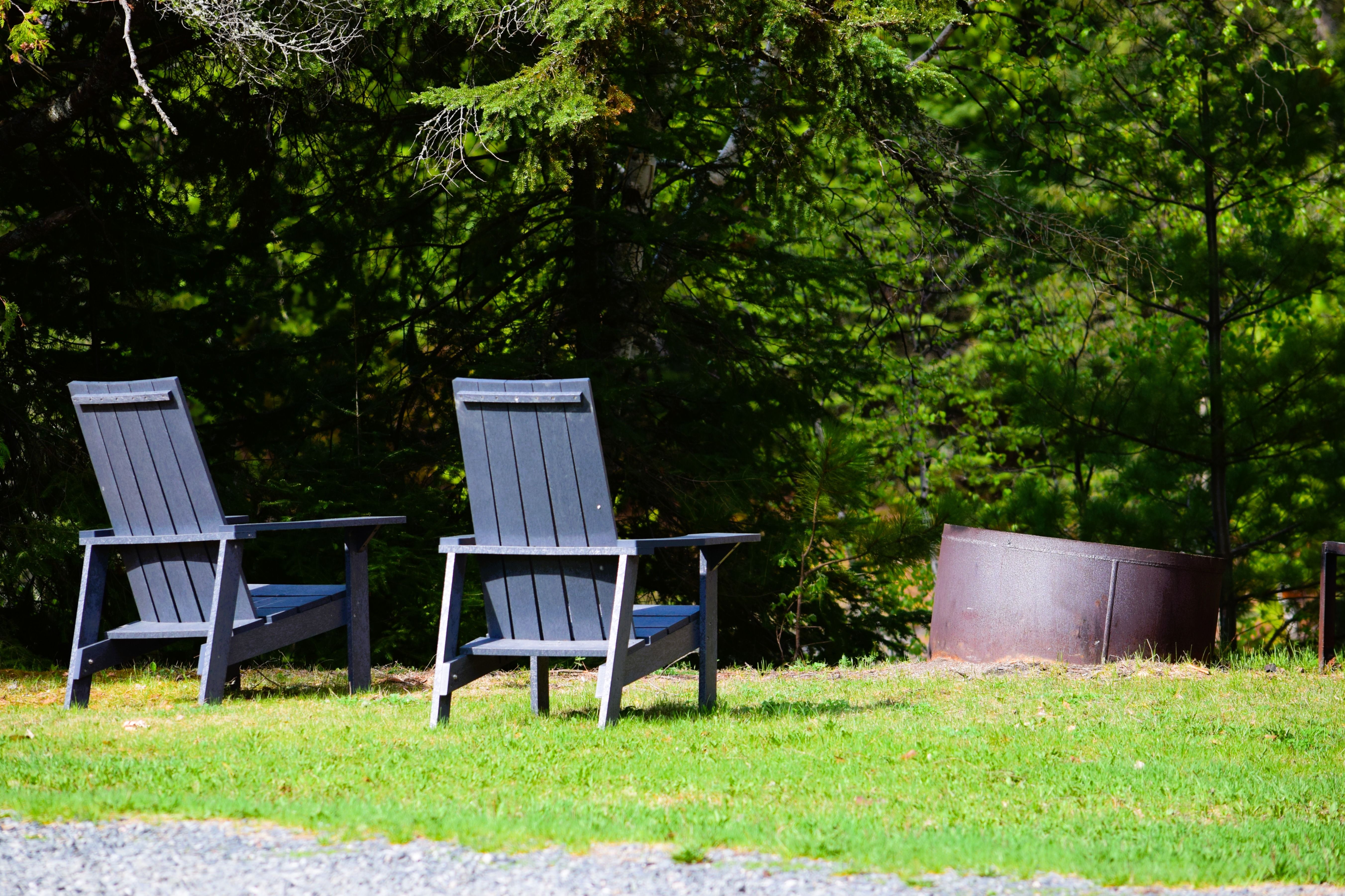 Adirondack chairs arranged around a fire pit in a peaceful outdoor lodge setting.