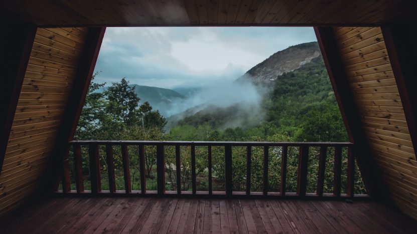 Wooden cabin balcony overlooking misty mountains and lush forest, illustrating a scenic outdoor living area.