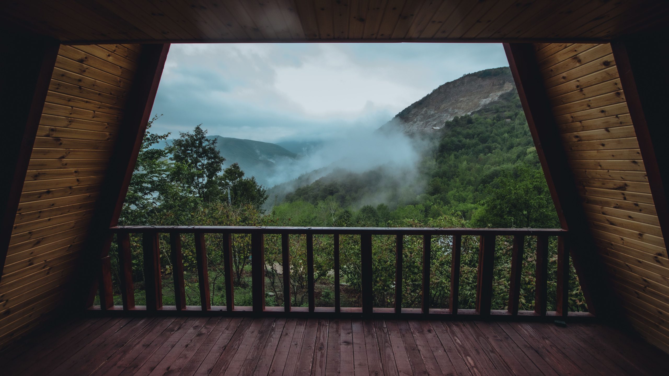 Wooden cabin balcony overlooking misty mountains and lush forest, illustrating a scenic outdoor living area.