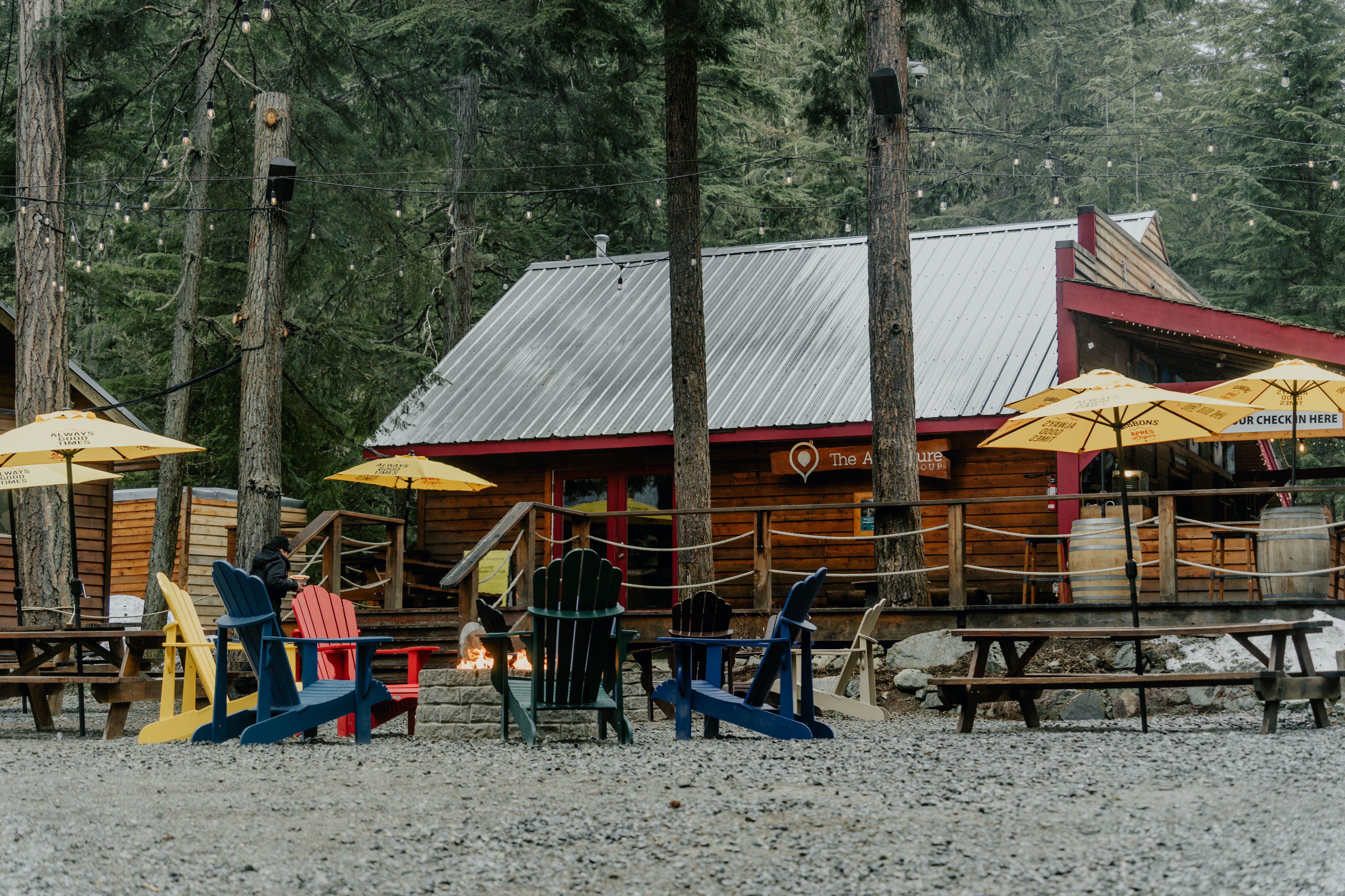 Colorful camp chairs and a campfire beside a rustic cabin at a wilderness campsite.